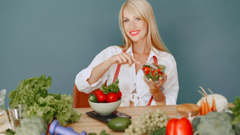 Blonde woman enjoying a fresh salad surrounded by vegetables, promoting healthy eating.